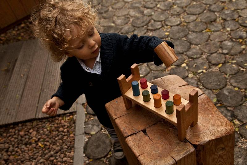 Kinder klopfen bunte Holzteile auf der Regenbogen Klopfbank – fördert Motorik